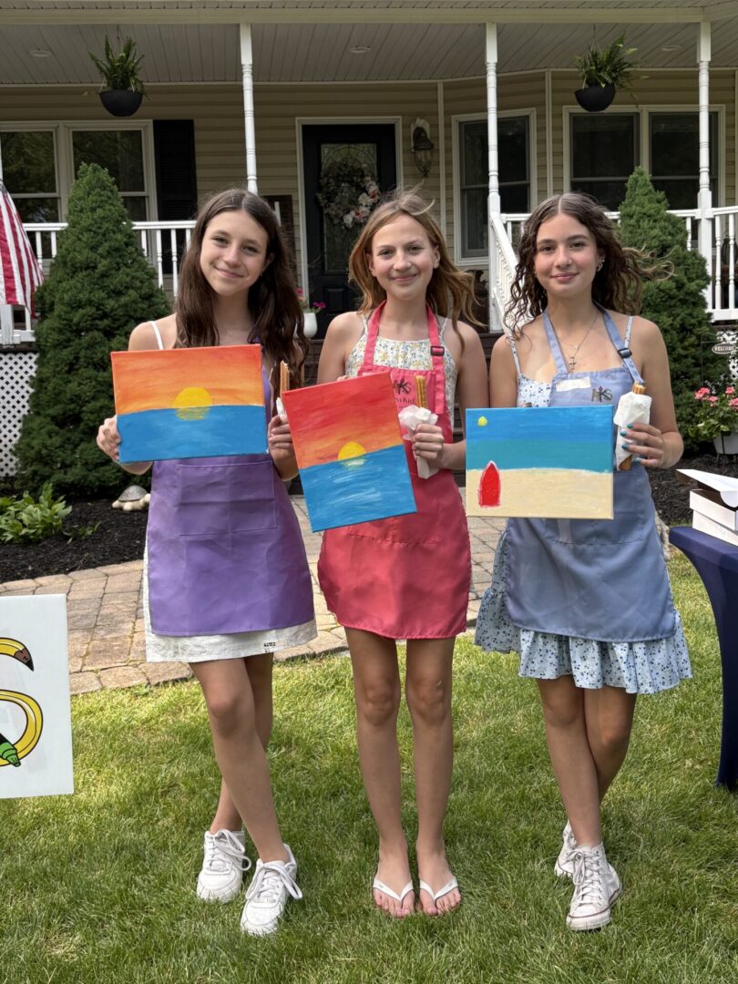 Three people holding painted sunset canvases