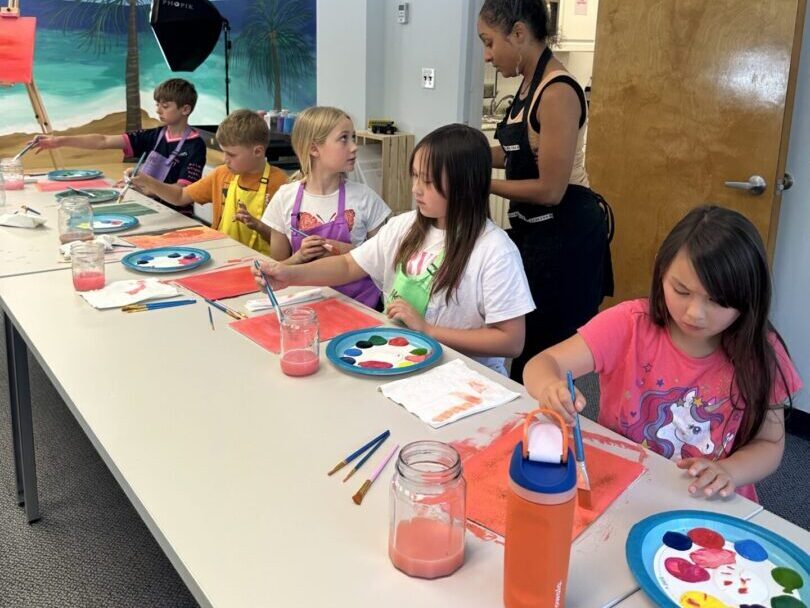 Children painting at long table in classroom