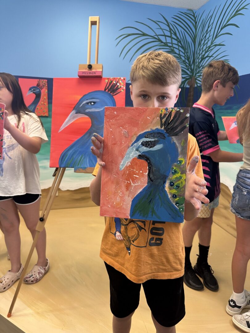 Child holding peacock painting in art class