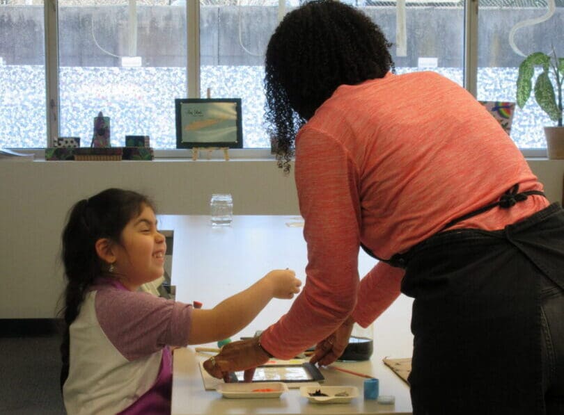 Girl smiling as instructor helps with painting