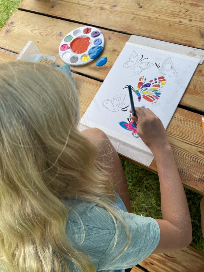 Child painting colorful butterflies at picnic table