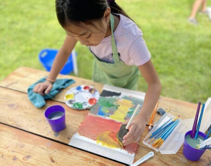 Child painting outdoors at wooden table