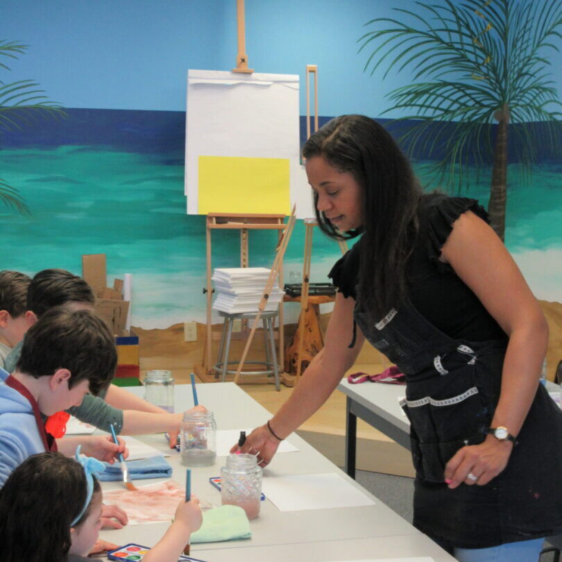 Art instructor guiding children painting at table